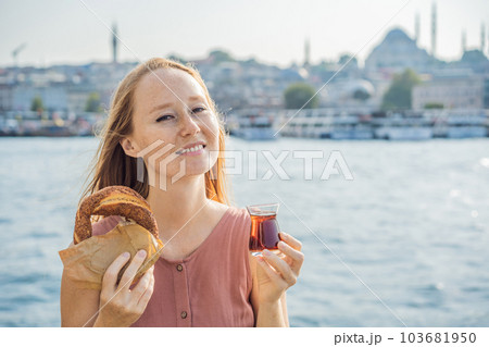 Woman in Istanbul having breakfast with Simit and a glass of Turkish tea. Glass of Turkish tea and bagel Simit against golden horn bay in Istanbul, Turkey. Turkiye 103681950