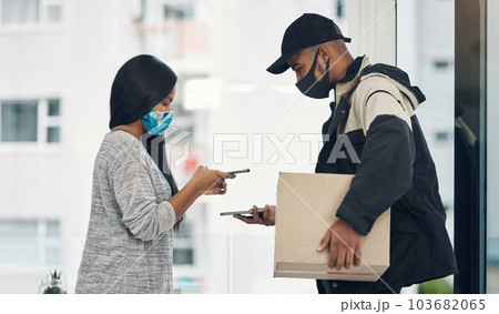 It just makes smarter sense to pay the contactless way. a masked young man and woman using smartphones during a home delivery. 103682065