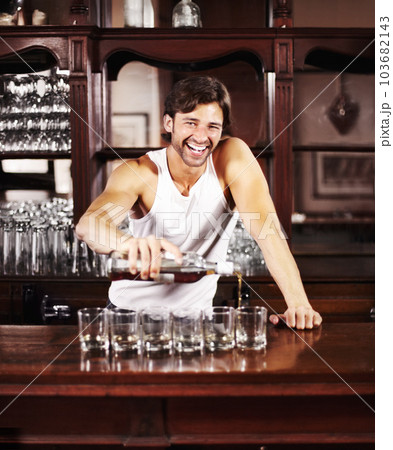 Portrait, whisky and alcohol with a handsome barman behind the counter of a pub to serve drinks during happy hour. Smile, glass and drink with a man bartender pouring a whiskey beverage in a bar 103682143