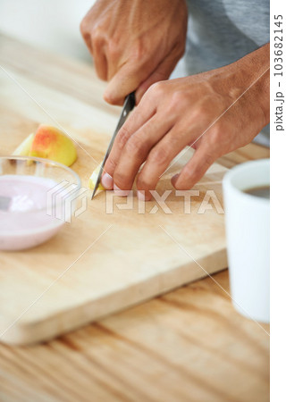 Slicing up some freshness. a man slicing an apple on a cutting board with a bowl of yogurt in front of him. 103682145