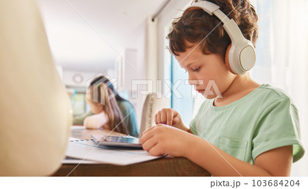Child, headphones and tablet for education and learning at a home table with internet connection. Boy kid using technology for educational mobile app, streaming video and movies or listening to sound 103684204