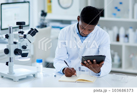 The research is paying off. a focused young male scientist browsing on a digital tablet while making notes inside of a laboratory. 103686373