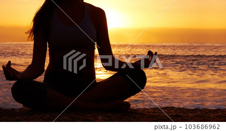 Silhouette, sunset and woman in lotus pose with yoga on the beach, orange sky and meditation outdoor. Healing, wellness and peace in nature with shadow, female yogi back and meditate by the ocean 103686962