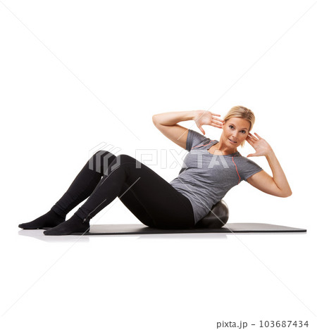 Giving her obliques workout. A young woman doing sit-ups on an exercise ball while isolated on a white background. Giving her obliques workout. A young woman doing sit-ups on an exercise ball while isolated on a white background. 103687434