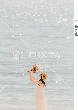海辺でドライフラワーを持って佇む女性 103688567