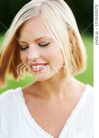 Sweet and naturally lovely. Gorgeous young woman looking downwards outdoors. 103688679
