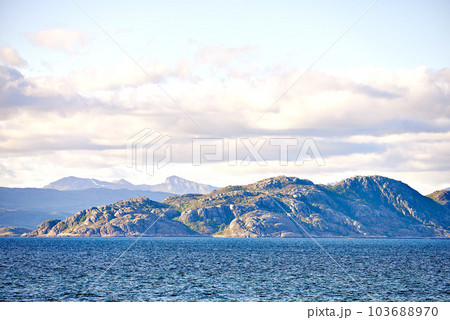 Scenic view of sea, mountains, rocks and boulders in Norway. Tidal ocean water waves, blue sky with clouds and copy space. Travel and tourism overseas and abroad to a remote and peaceful destination 103688970