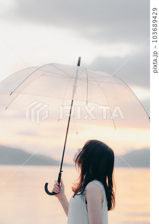 夕焼けに傘をさしてる女性 103689429