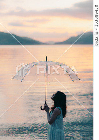 夕焼けに傘をさしてる女性 103689430