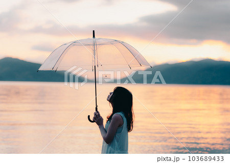 夕焼けに傘をさしてる女性 103689433