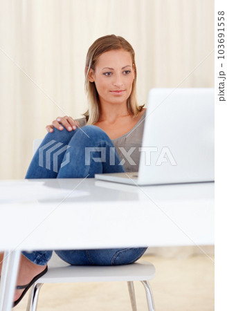 Just browsing away the day. A young woman sitting at her desk and looking at her laptop screen. 103691558