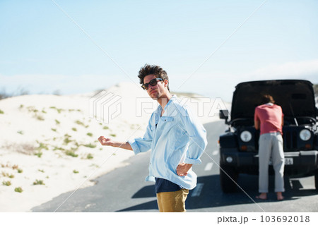 I guess well have to hitchhike. A young man trying to hitch a ride while his friend looks at the engine in the background. 103692018