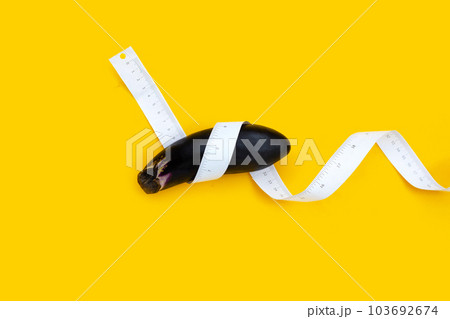 Measuring tape around eggplant on yellow background. Measuring tape around eggplant on yellow background. 103692674