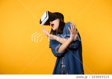 Young asian woman get experienced wearing virtual reality headset game entertainment isolated on yellow background. Winner of cyber future video game concept. Young asian woman get experienced wearing virtual reality headset game entertainment isolated on yellow background. Winner of cyber future video game concept. 103693525