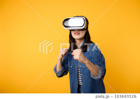 Young asian woman get experienced wearing virtual reality headset game entertainment isolated on yellow background. Winner of cyber future video game concept. Young asian woman get experienced wearing virtual reality headset game entertainment isolated on yellow background. Winner of cyber future video game concept. 103693526