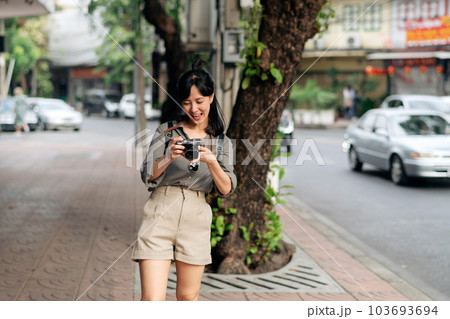 Young Asian woman backpack traveler using digital compact camera, enjoying street cultural local place and smile. Traveler checking out side streets. 103693694