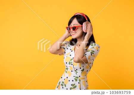 Smile pretty asian model person listen music song and enjoy dance with wireless headphone online audio radio sound. Positive fun exited joyful youth female woman on yellow isolated background studio 103693759
