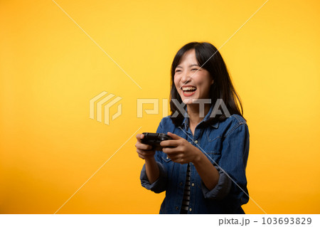 Portrait young asian woman with happy success smile wearing denim clothes holding joystick controller and playing video game. Fun and relax hobby entertainment lifestyle concept. Portrait young asian woman with happy success smile wearing denim clothes holding joystick controller and playing video game. Fun and relax hobby entertainment lifestyle concept. 103693829