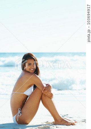 Shes a cute beach babe. A gorgeous young woman sitting on the beach. Shes a cute beach babe. A gorgeous young woman sitting on the beach. 103694917
