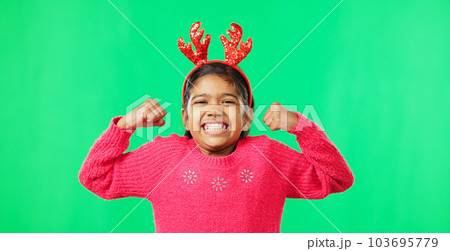 Child portrait, christmas and antlers on green screen flexing strong muscles or arms for motivation. Smile on face of a girl kid on a studio background with reindeer headband for holiday celebration Child portrait, christmas and antlers on green screen flexing strong muscles or arms for motivation. Smile on face of a girl kid on a studio background with reindeer headband for holiday celebration 103695779