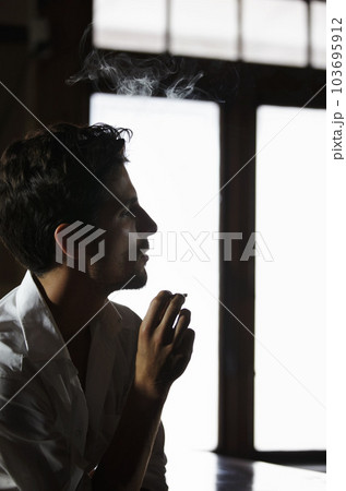 Smoking, man and thinking in pub with cigarette or male model or vapor customer and smoker unhealthy on bokeh. Habit, addiction and male person with tobacco or in thought or relaxing and in a club 103695912