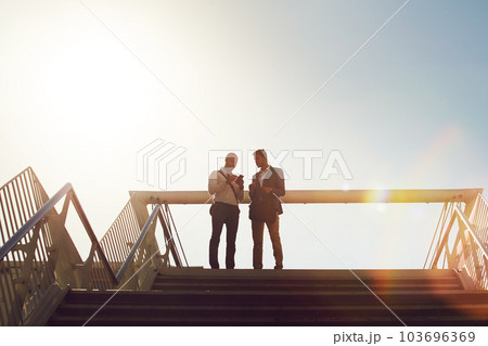 Lets set up an appointment to discuss ideas. Low angle shot of two businessmen using a cellphone on top of a staircase outside. 103696369