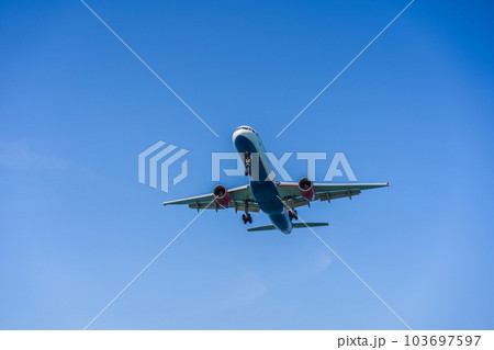 A white airplane flying in a clear pale blue sky 103697597