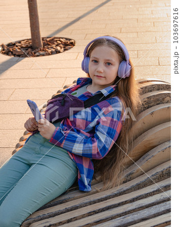 Blonde child in headphones listening to music podcast smartphone outside Young girl learn online lesson enjoy audio book Blonde child in headphones listening to music podcast smartphone outside Young girl learn online lesson enjoy audio book 103697616