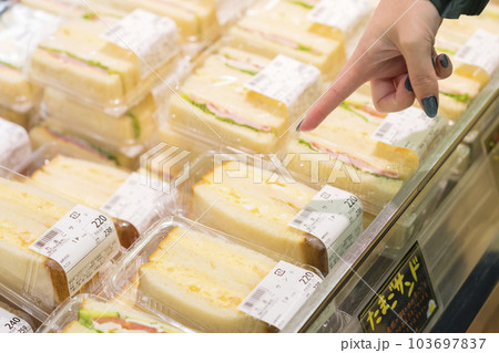 スーパーの売り場にあるサンドウィッチをさす若い女性手元 スーパーの売り場にあるサンドウィッチをさす若い女性手元 103697837