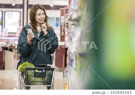 スーパーでスマホを見ながら買い物をする若い女性 103698385