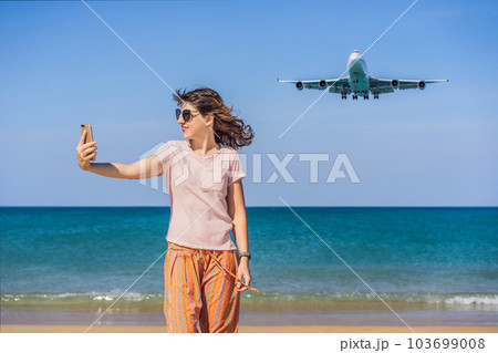 Woman makes a selfie on the beach watching the landing planes. Traveling on an airplane concept. Text space. Island Phuket in Thailand. Impressive paradise. Hot beach Mai Khao. Amazing landscape 103699008