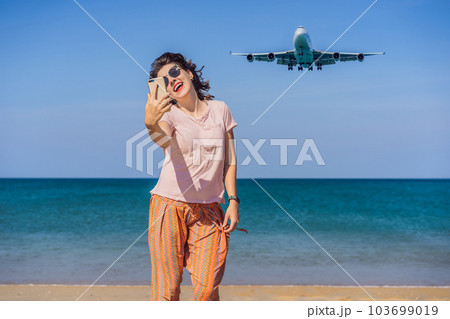 Woman makes a selfie on the beach watching the landing planes. Traveling on an airplane concept. Text space. Island Phuket in Thailand. Impressive paradise. Hot beach Mai Khao. Amazing landscape 103699019