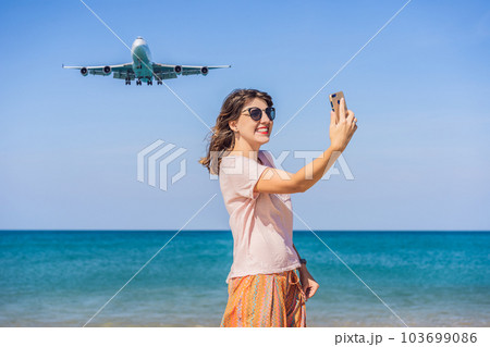 Woman makes a selfie on the beach watching the landing planes. Traveling on an airplane concept. Text space. Island Phuket in Thailand. Impressive paradise. Hot beach Mai Khao. Amazing landscape 103699086