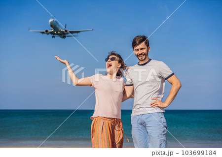 Man and woman tourists have fun on the beach watching the landing planes. Traveling on an airplane concept. Text space. Island Phuket in Thailand. Impressive paradise. Hot beach Mai Khao. Amazing 103699184