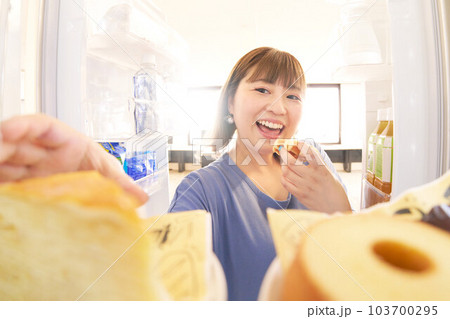 冷蔵庫を開けてケーキを取ろうとする若い女性 冷蔵庫を開けてケーキを取ろうとする若い女性 103700295