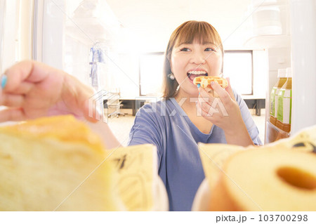 冷蔵庫を開けてケーキを取ろうとする若い女性 冷蔵庫を開けてケーキを取ろうとする若い女性 103700298