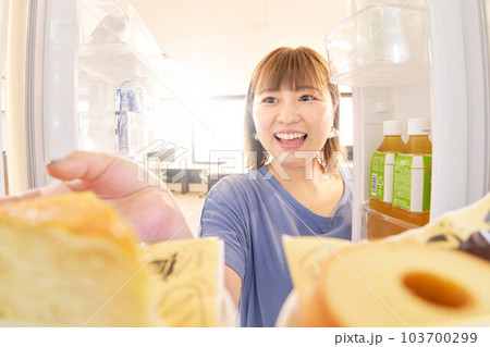 冷蔵庫を開けてケーキを取ろうとする若い女性 103700299