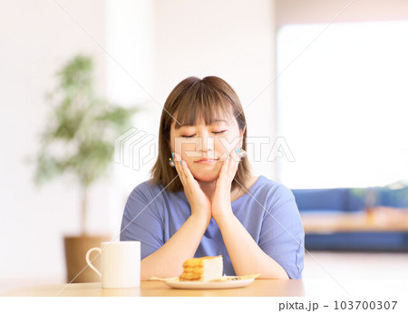 テーブルの上に置いたケーキを見つめる若い女性 103700307