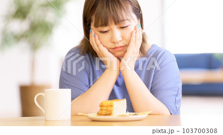テーブルの上に置いたケーキを見つめる若い女性 103700308