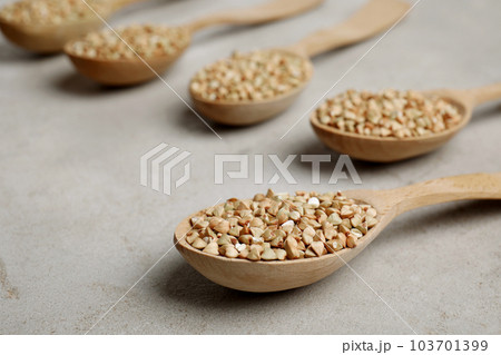 Uncooked green buckwheat grains in spoons on light table 103701399
