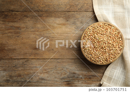 Uncooked green buckwheat grains in bowl on wooden table, top view. Space for text 103701751