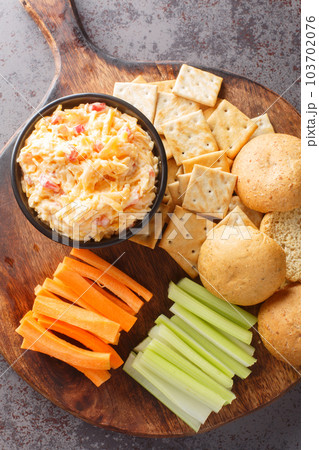 Pimento cheese is a popular Southern spread made with shredded Cheddar, mayonnaise, and pimentos served on crackers and vegetables closeup on the wooden board. Vertical top view Pimento cheese is a popular Southern spread made with shredded Cheddar, mayonnaise, and pimentos served on crackers and vegetables closeup on the wooden board. Vertical top view 103702076