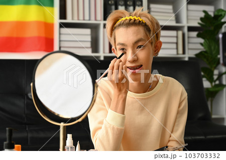 Young asian man applying concealer under his eyes with cosmetics brush. LGBTQ lifestyle, beauty and cosmetic 103703332