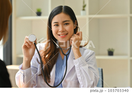 Positive female doctor in white coat holding stethoscope and looking at camera. Healthcare and medical concept Positive female doctor in white coat holding stethoscope and looking at camera. Healthcare and medical concept 103703340