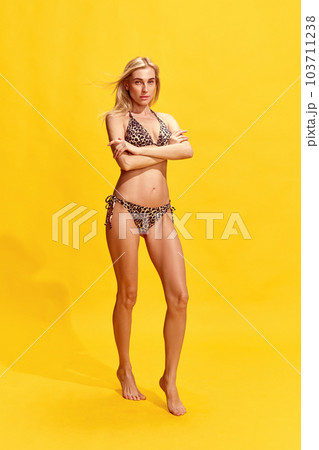 Beautiful young woman with perfect, slim, tanned body in stylish swimsuit against yellow studio background Beautiful young woman with perfect, slim, tanned body in stylish swimsuit against yellow studio background 103711238