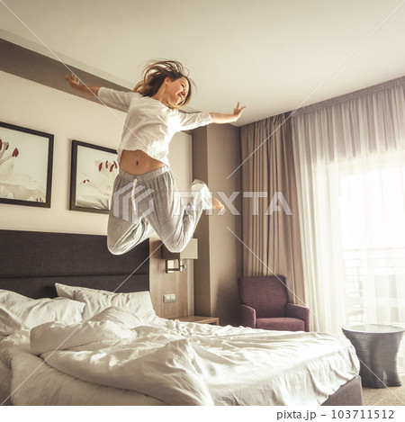 Woman having fun and jumping with bathrobe on bed in hotel room 103711512