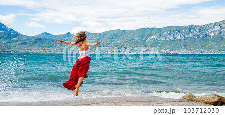 Woman in red dress jumping at the lake 103712030