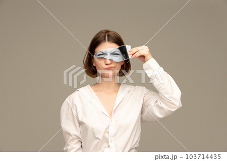 Young girl with funny grimace face holding photo part with eyes looking attentively. Creative collage. 103714435