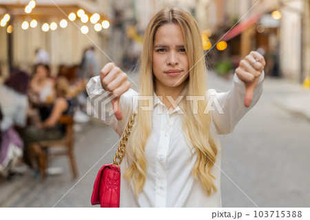 Upset young woman girl showing thumbs down sign, disapproval, dissatisfied bad work, mistake in city Upset young woman girl showing thumbs down sign, disapproval, dissatisfied bad work, mistake in city 103715388