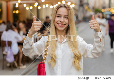 Happy woman showing thumbs up, like sign positive something good positive feedback in city street Happy woman showing thumbs up, like sign positive something good positive feedback in city street 103715389